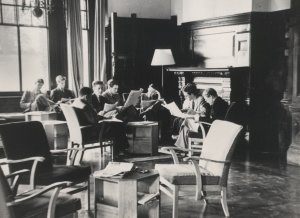 Black and white photo of eight students reading papers sitting in a common room in Manor House in the 1940s