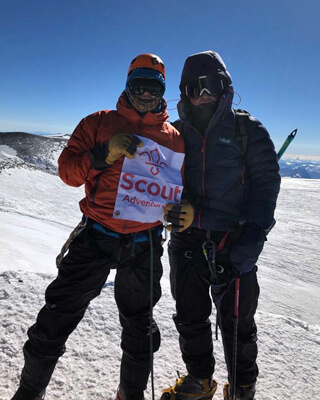 Jack Garner (right) and guide Paul Etheridge at the top of Mount Elbrus holding a 'Scout adventure' sign